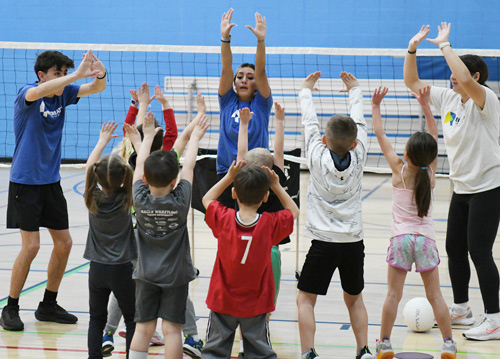 Greeley Rec staff guiding a group of children in learning volleyball techniques indoors.