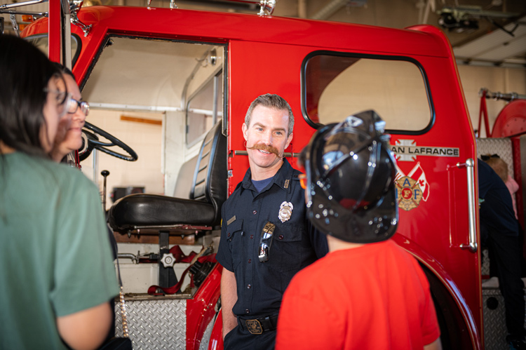 A firefighter introduces visitors to a fire truck during an open house event, showcasing firefighting equipment and engaging with the community.
