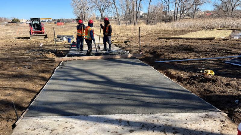 Three workers pour concrete to create a new walking path in a park area.