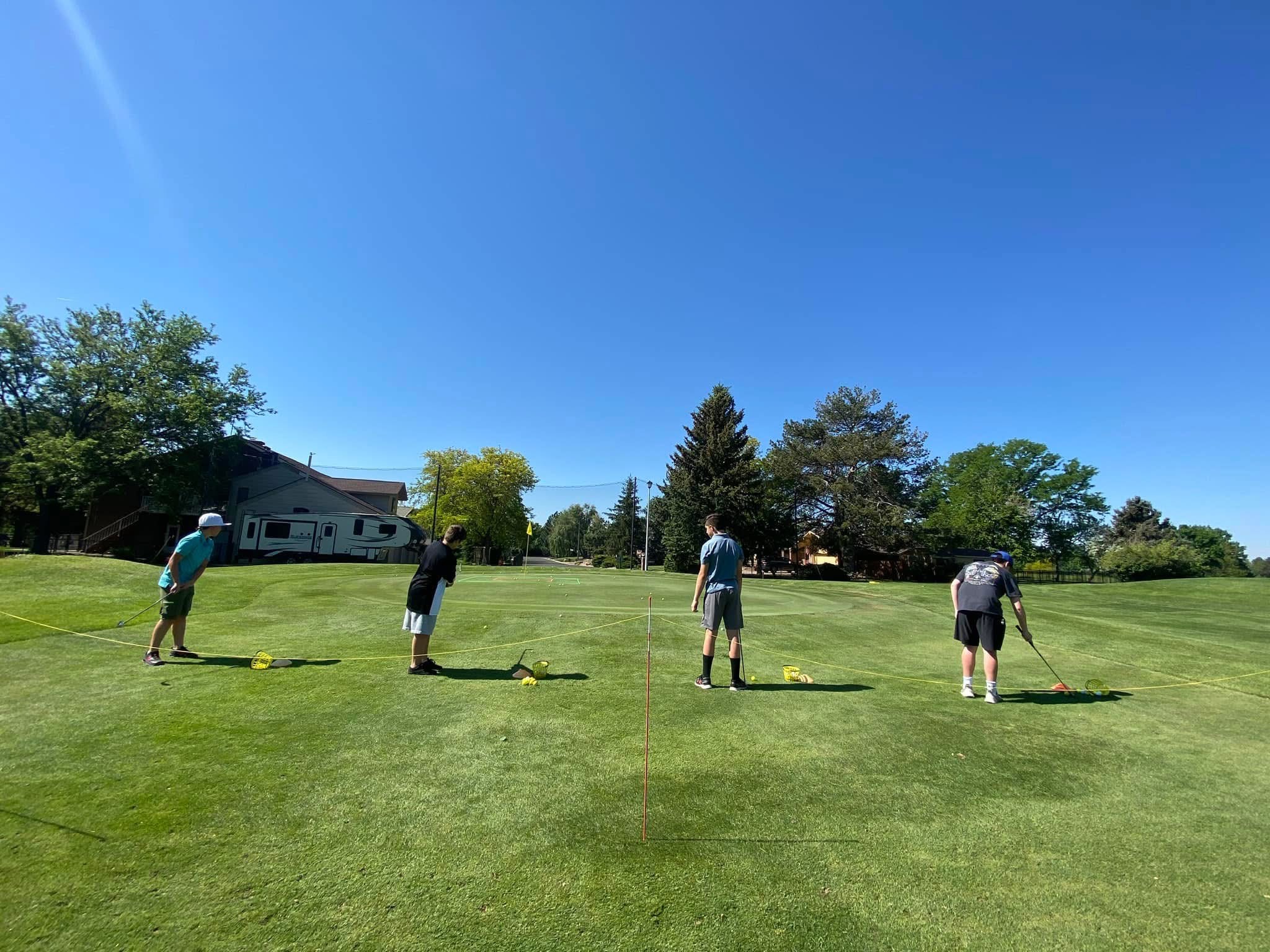Four junior golfers practicing on a green golf course under a clear blue sky.