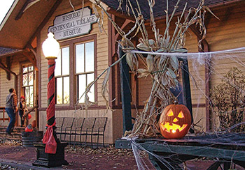 A decorated historic museum showcasing festive Halloween decorations, including carved pumpkins, corn stalks, and cobwebs, with families enjoying the scene.