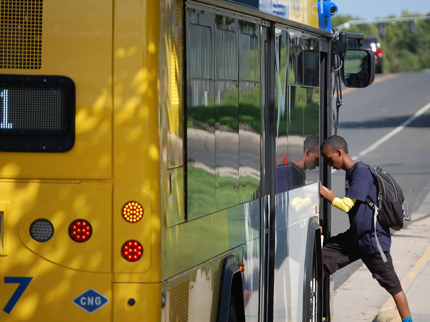 A young student wearing a backpack steps onto a bus