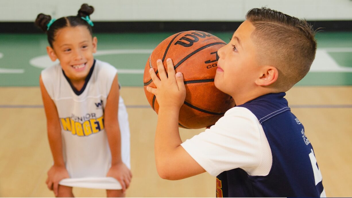 A young boy prepares to shoot a basketball while a friend looks on during a practice session.