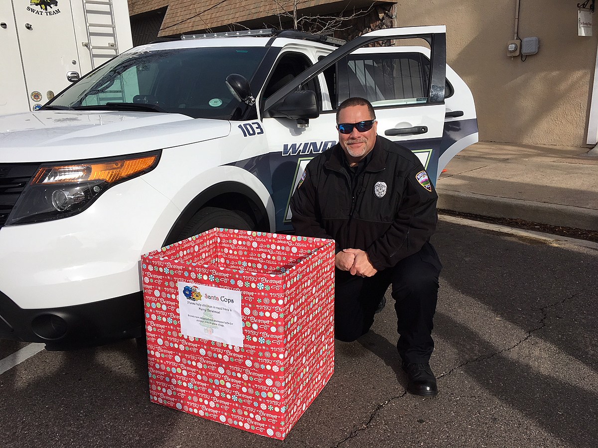 A Windsor police officer showcases a festive donation box as part of the Santa Cops program aimed at community support.
