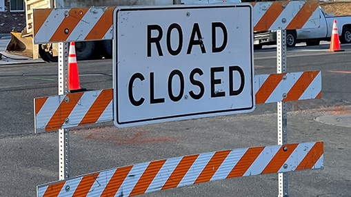 A road closed sign with orange and white stripes indicating restricted access during construction activities.