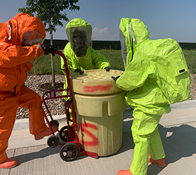 Three Greeley firefighters carefully manage a drum of hazardous material during a safety operation.