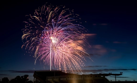 Fireworks burst vividly over a stadium during twilight, showcasing vibrant colors against the night sky.