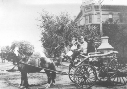 Old black and white photo of the Greeley Fire Department, featuring a horse-drawn firefighting wagon in front of a historic building.