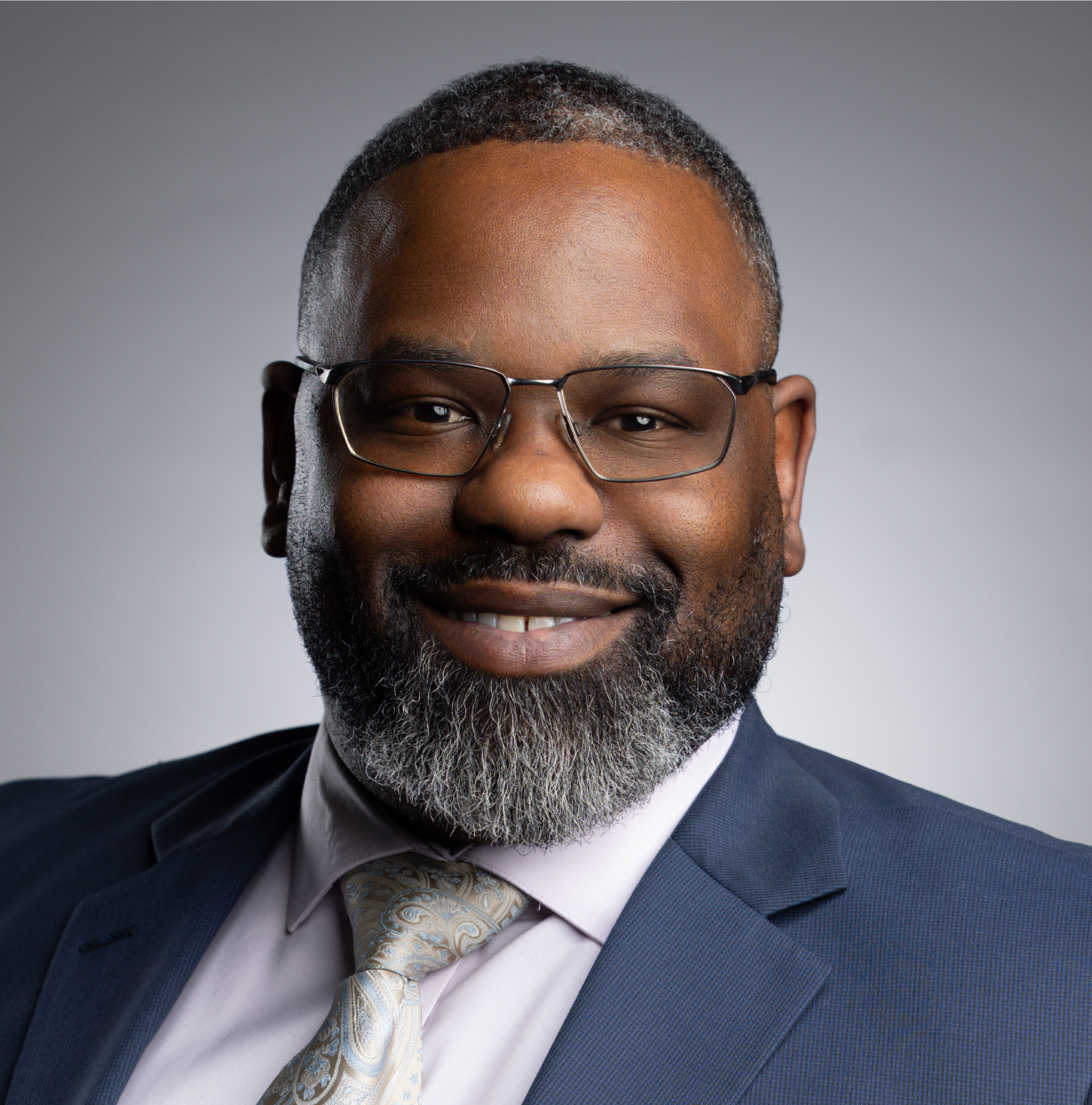 This image depicts a professional headshot of Workforce Development Manager Robert Thompson.  Robert is shown in a glasses, a gray suit jacket, lavender dress shirt, and matching paisley tie.  
