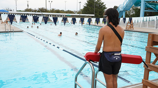 Lifeguard watches over swimmers in the outdoor pool on a summer day