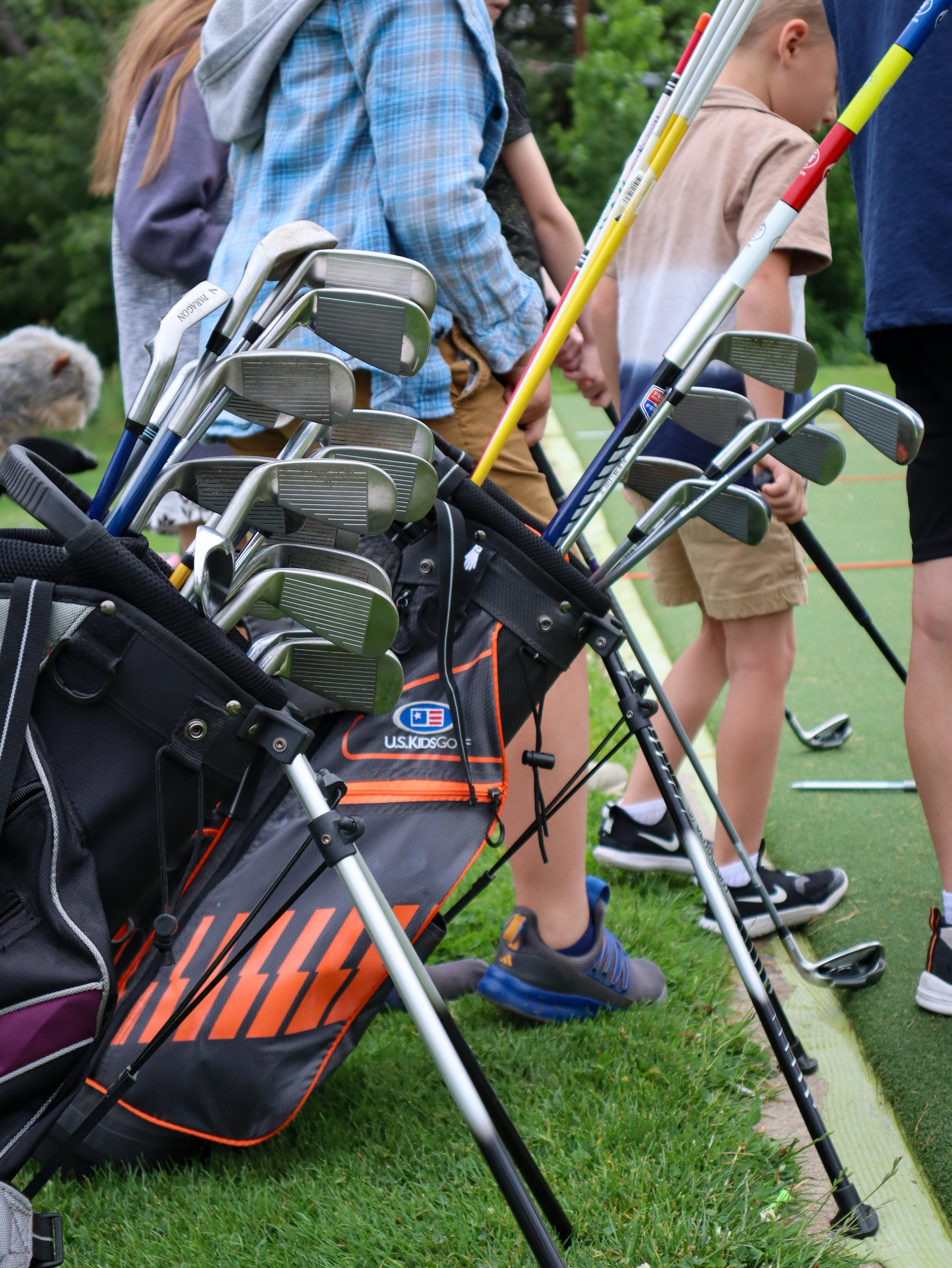 Golf bags filled with clubs as children listen and participate in a junior golf clinic.