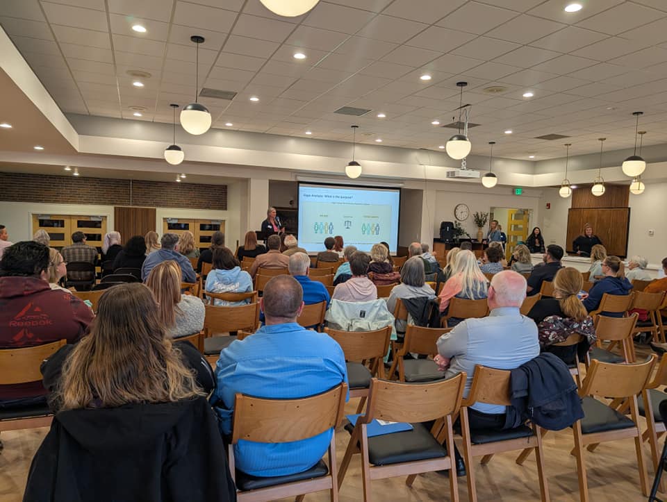 A group of people sitting in chairs facing the front of the room looking at a presentation given by Director of the Homeless Solutions department Mandy Shreve. 