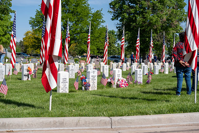 White headstones adorned with small American flags and people standing in front of soldiers’ graves