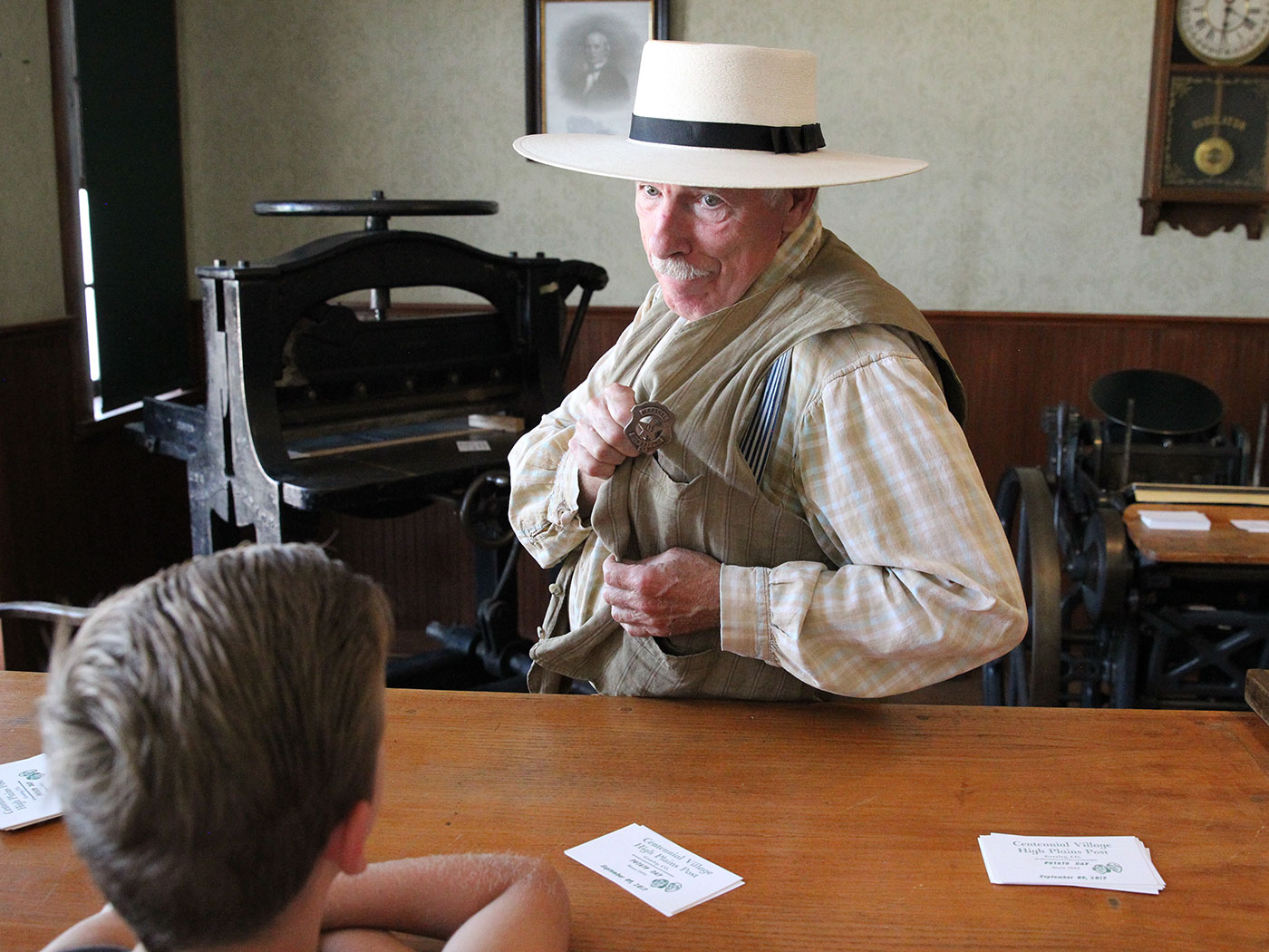 Older gentleman dressed in historic clothing shows his marshall badge to a boy in a room with historic paintings and furnishings