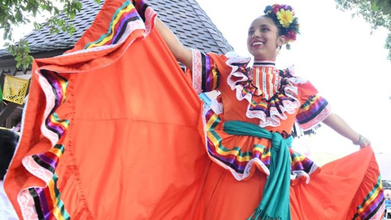 A vibrant display of Mexican cultural heritage with a dancer showcasing her colorful skirt on the plaza at Centennial Village Museum.