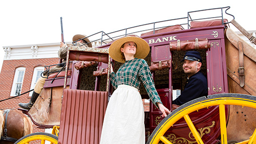A group of individuals dressed in period attire by a vintage stagecoach, evoking a historical atmosphere.
