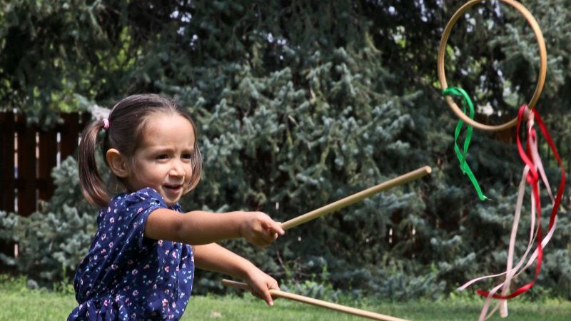A child actively participates in a traditional outdoor game using sticks and a decorated wooden hoop.