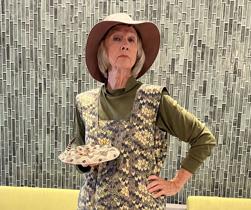 Tannis Bator strikes a pose while wearing a replica rattlesnake dress and holding a fake rattlesnake in her hand.