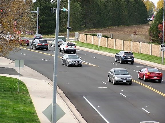 A busy roadway surrounded by greenery, featuring multiple cars traveling along a renovated street.
