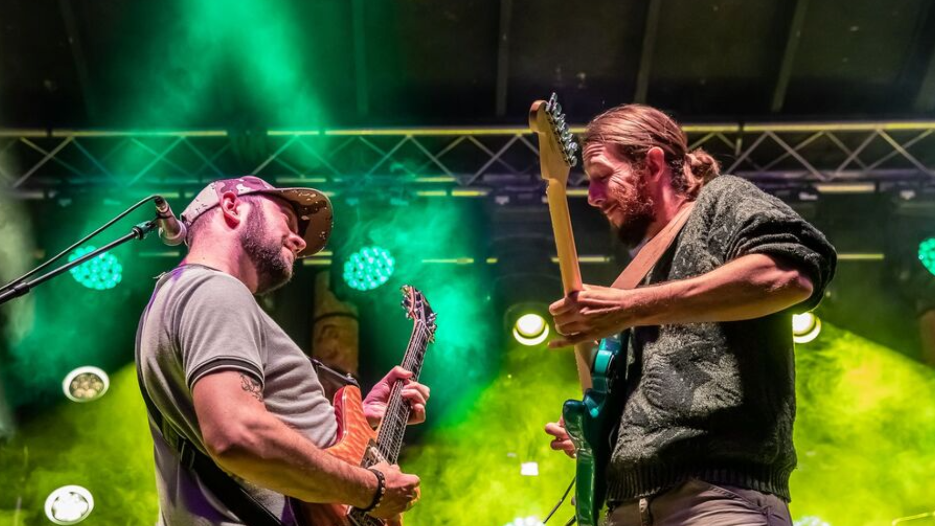 Tumbledown Shack band photo. Two musicians on stage with guitars and bright green stage lights surrounding.  The band will play Friday Fest for Culture Pop/Arts Picnic 2026.