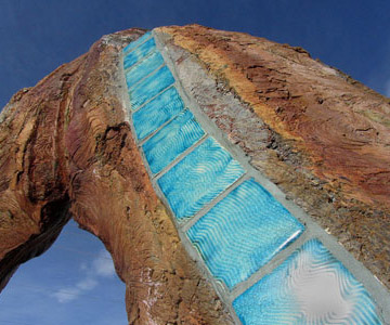 An artistic representation featuring textured stone and shimmering blue glass elements with a backdrop of clear skies.