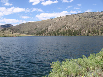 A serene view of the Milton Seaman Reservoir surrounded by hills and greenery under a bright sky.