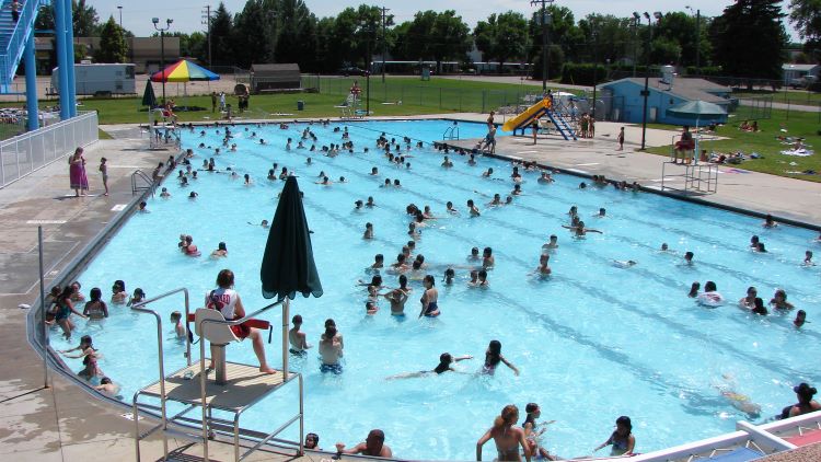 View of families and residents swimming and enjoying the outdoor Centennial Pool in Greeley surrounded by green lawns.