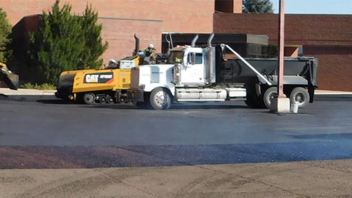 Construction vehicles engaged in road maintenance on a city street with visible equipment and workers.