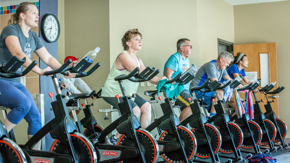 Six adults sitting on stationary bikes during a spinning class workout at the Family FunPlex