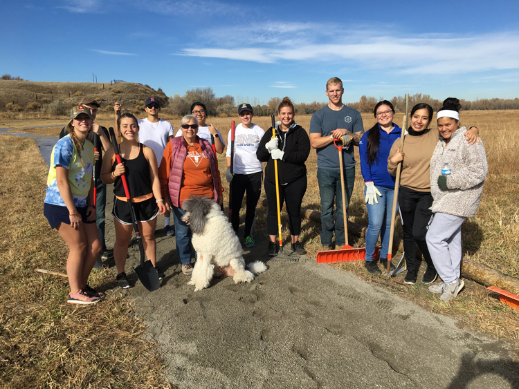 Group of volunteers gathered outdoors with tools to participate in a local clean-up initiative on a sunny day.