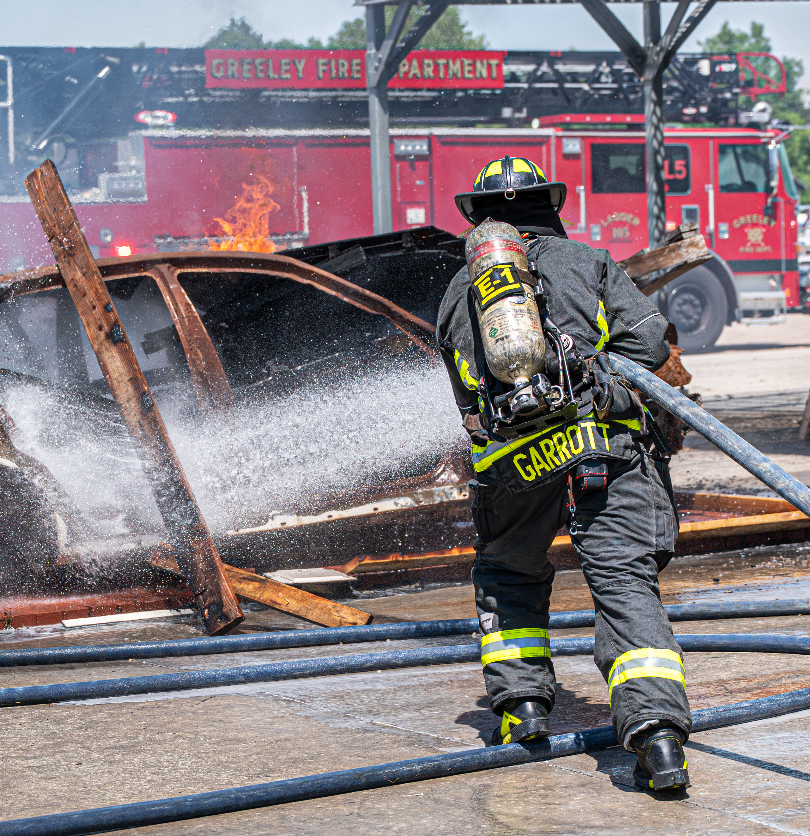 Firefighter sprays water from a hose line onto a car that is on fire. 