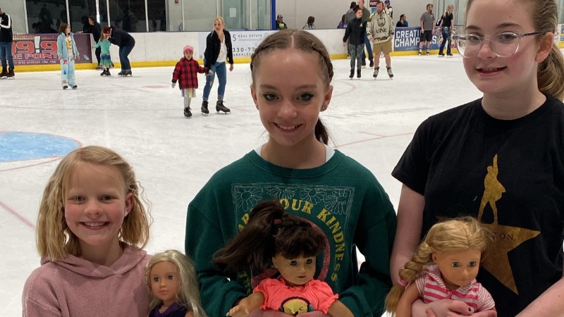 Three girls holding their dolls at the Ice Haus rink during the American Girl Doll Skate event.