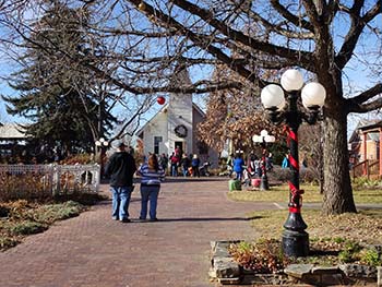 A serene view of people enjoying a walk in a historic village setting surrounded by trees and festive decorations.