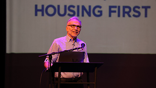 A speaker presenting key insights about the Housing First program at a community forum.