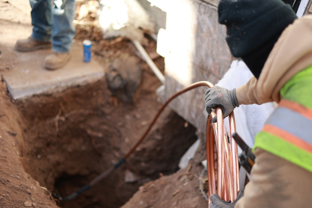 A worker uncoils copper pipe as it is laid in a trench.