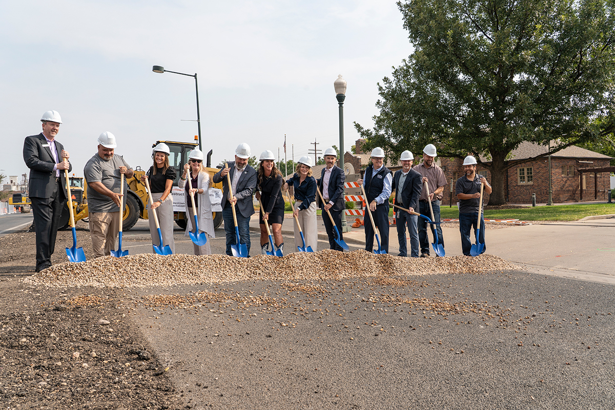 People wearing hard hats hold shovels as they break ground on new infrastructure build. 