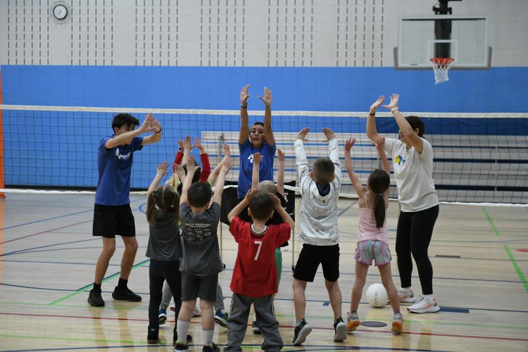 Volunteer coaches guide children in a recreational volleyball activity, emphasizing teamwork and learning.