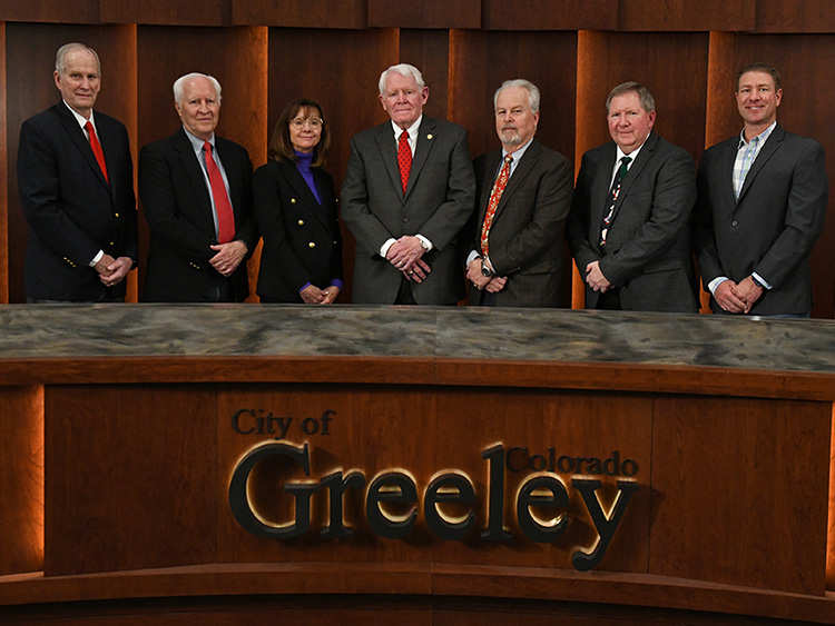 A group photo of the City Council members of Greeley, Colorado, standing behind a wooden podium.