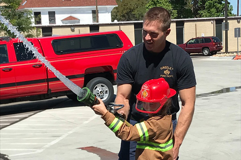 A young firefighter practicing firehose techniques guided by an experienced trainer.
