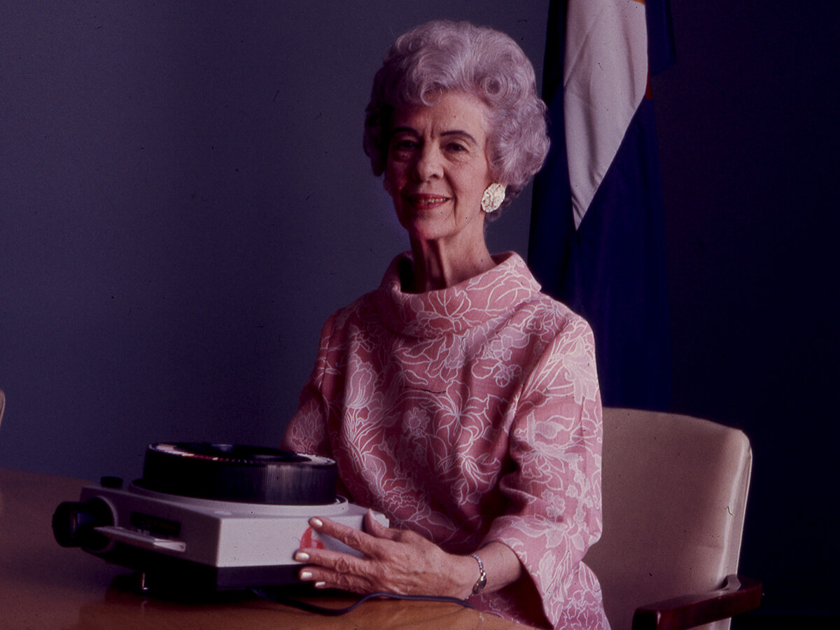 Portrait of Hazel E Johnson sitting at a table and holding a film projector