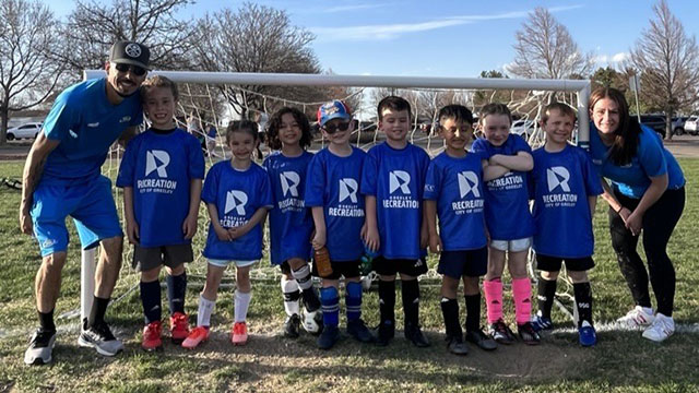 Volunteer soccer coaches pose with their team after a game in front of the goal