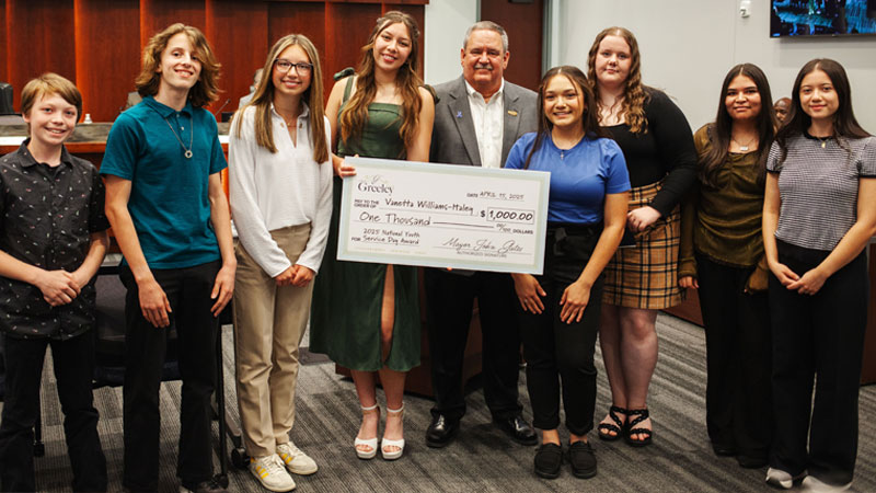Mayor presenting scholarship to a high school student at City Council meeting for national award.