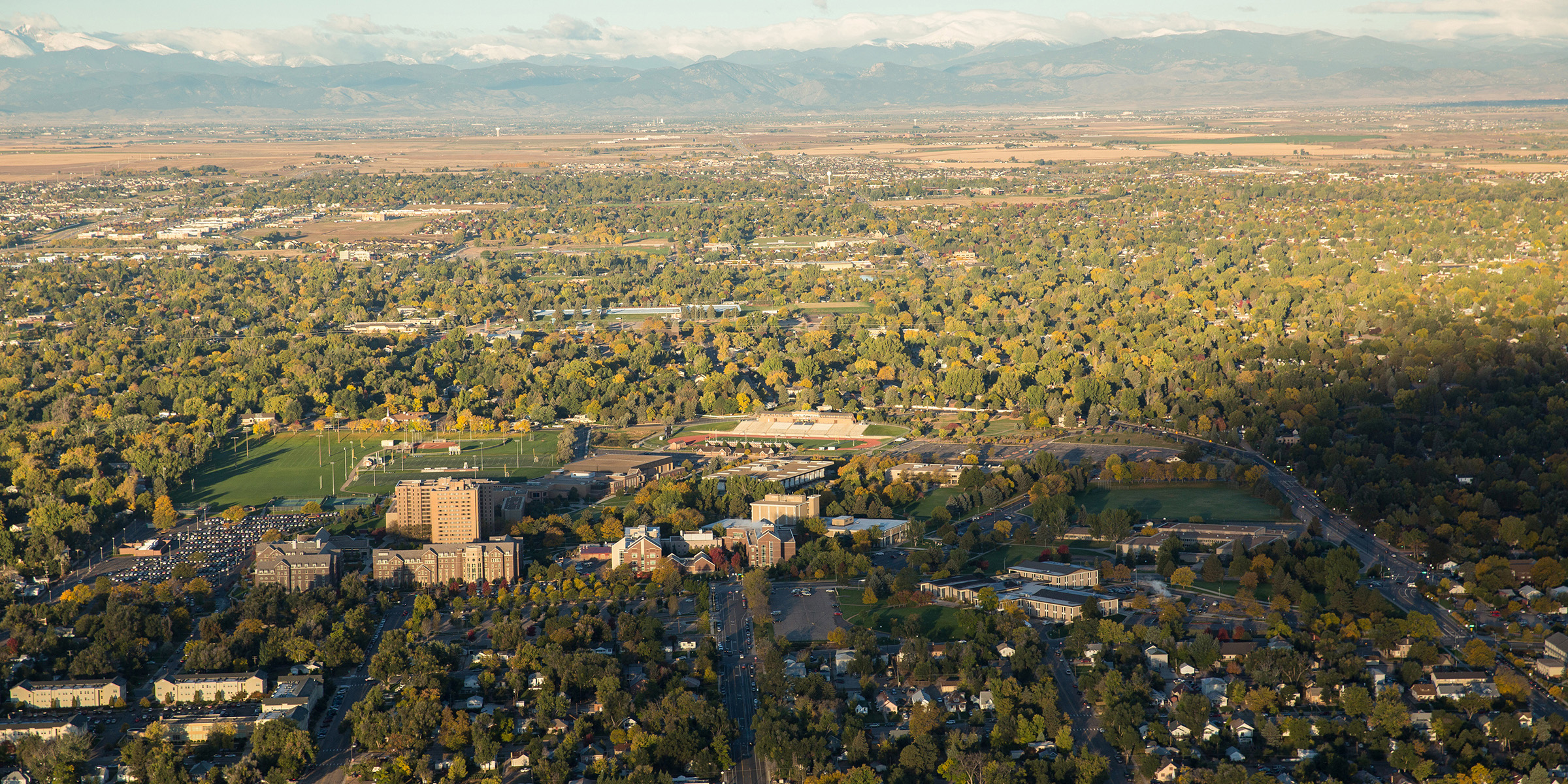 A scenic aerial image showcasing the University of Northern Colorado campus surrounded by greenery and urban landscape extending towards the horizon.