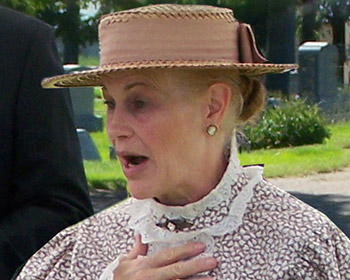 A person dressed in a vintage outfit featuring intricate patterns and a woven hat, possibly participating in a historical reenactment or event.