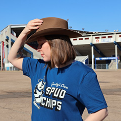 A person wearing a blue t-shirt showcasing Greeley's Own Spud Chips design with a cartoon potato in cowboy attire.