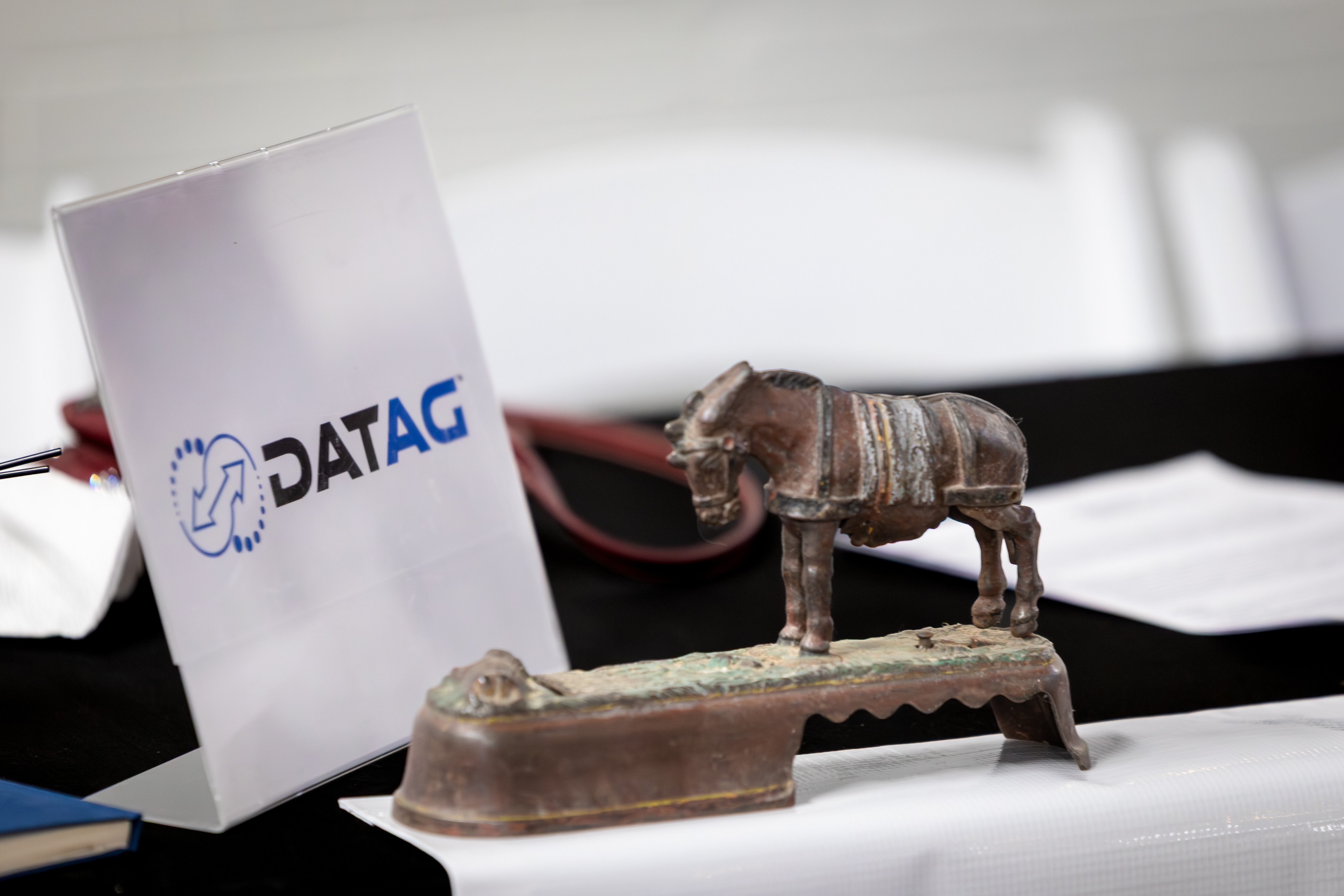 Display table with a DATAG sign and logo, with a small antique horse figurine on a metal base.