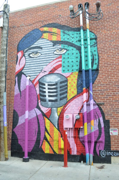 A vibrant mural in a downtown alleyway showcasing a colorful design of a singer with a microphone, blending modern patterns and bold lines.