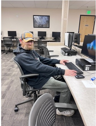 Aaron sitting in a chair at a computer in a computer lab. 