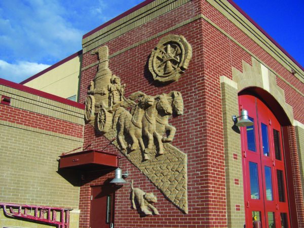 Exterior view of a fire station featuring brick architecture with sculpted artwork of historical firefighting scenes.