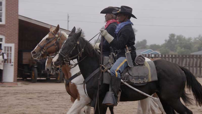 A scenic representation of Buffalo Soldiers riding horses at the Centennial Village Museum, showcasing historical reenactments.